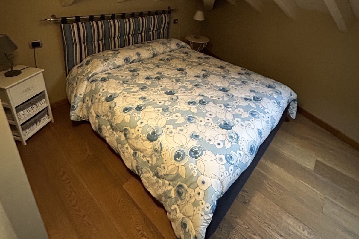 A bedroom with a sloped ceiling, a bed with floral bedding, a nightstand, and a lamp.