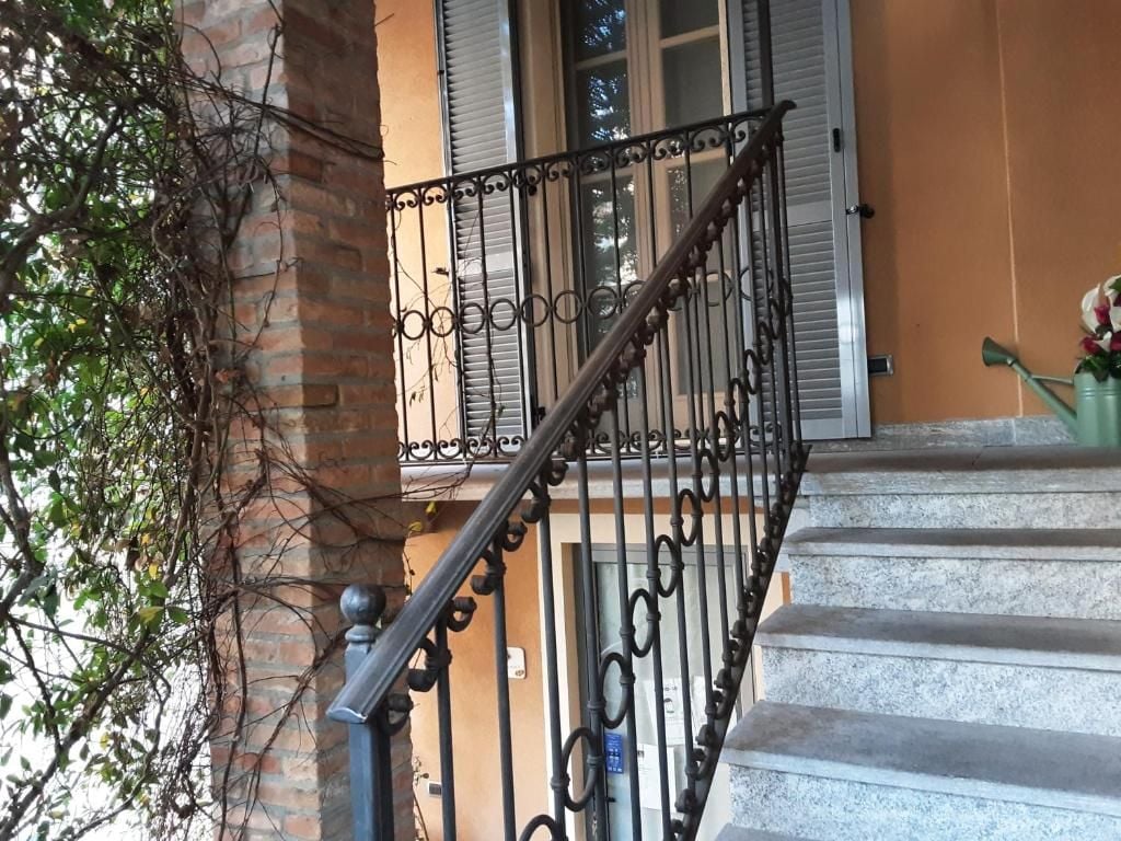 Un escalier avec une rampe en fer forgé, une colonne en briques et une fenêtre avec des volets.