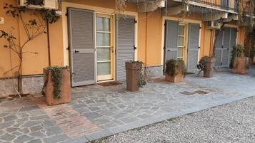 A building with closed shutters, potted plants, and a stone-paved ground.