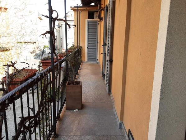 A narrow outdoor corridor with a metal railing, potted plants, and a door leading to an interior space. - B&B Corte delle Rose (Voghera)