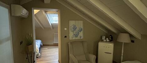 A cozy attic bedroom with a sloped ceiling, a wooden floor, a bed, a chair, a small table with a vase, and a radiator.