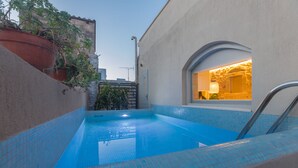 A small outdoor swimming pool with blue tiled edges, a potted plant on the left, and a window with a light fixture on the right. - In the old historical town of Rethymno,Daphne Luxury Home with a private pool (Rethymno)
