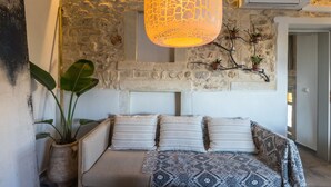 A cozy bedroom with a stone wall, a hanging lamp, a bed with patterned bedding, and a potted plant. - In the old historical town of Rethymno,Daphne Luxury Home with a private pool (Rethymno)