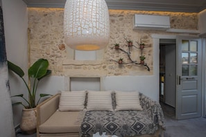 A room with a stone wall, a sofa with cushions, a hanging light fixture, and a small plant on a shelf.