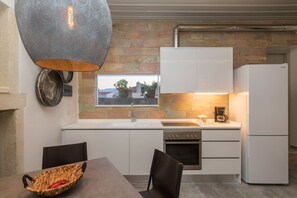 Une cuisine moderne avec des armoires blanches, un four encastré, un réfrigérateur blanc et un luminaire suspendu.
