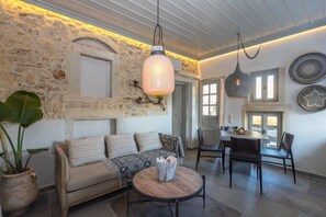 Un salon chaleureux avec un mur en pierre, un canapé, une table basse et un coin repas comprenant des chaises et une table.