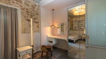 A bedroom with a stone wall, a bedside table, a mirror, a bed, and a glass door leading to another room.