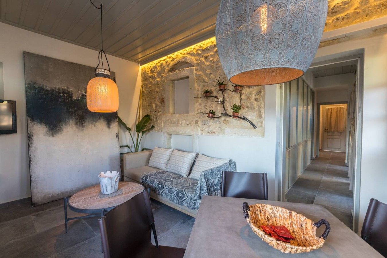 A modern interior with a stone wall, a round table with a woven basket, and a sofa with patterned cushions.