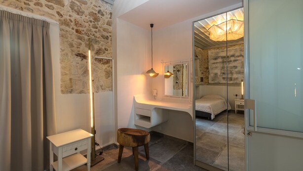 A modern bedroom with a stone wall, a bedside table, a mirror, and a bed. - In the old historical town of Rethymno,Daphne Luxury Home with a private pool (Rethymno)