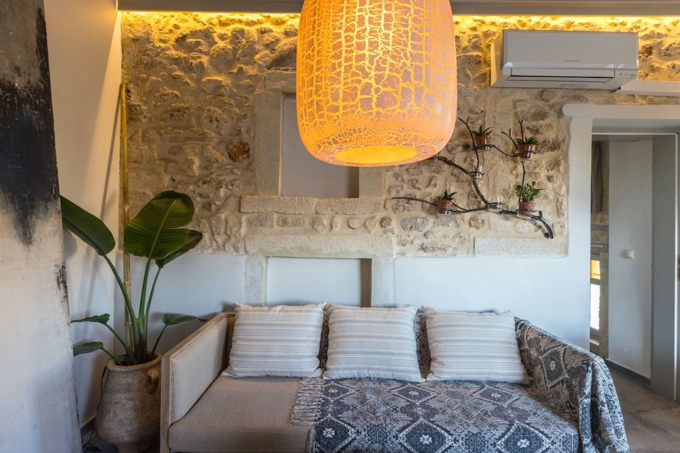 A cozy bedroom with a stone wall, a hanging lamp, and a bed with patterned bedding.