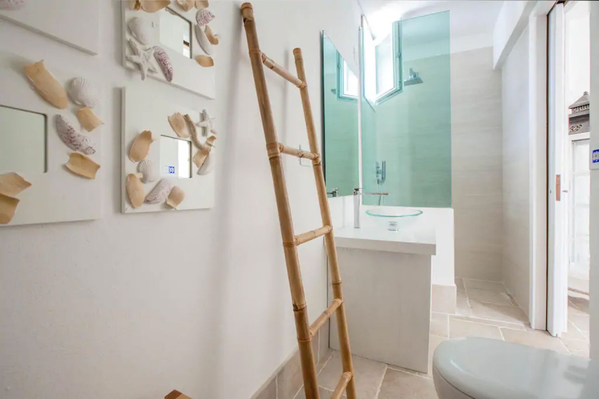 Baño con escalera de bambú, inodoro y lavabo de vidrio.