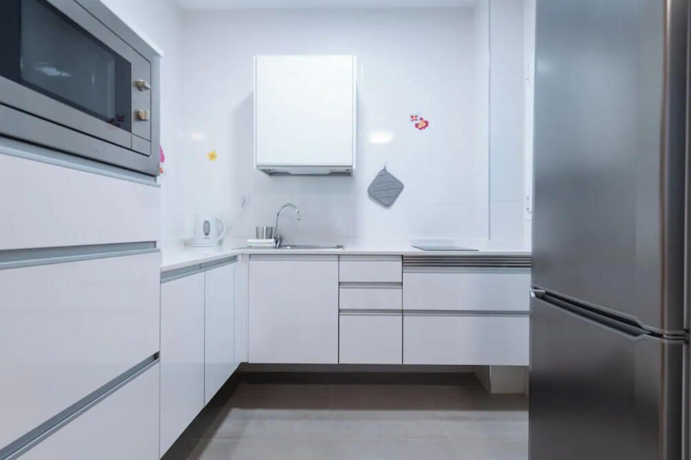 Una cocina moderna con armarios blancos, un refrigerador de acero inoxidable y un microondas.