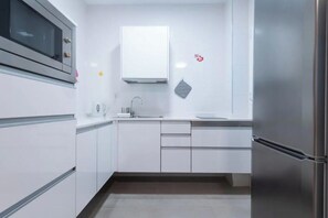 A modern kitchen with white cabinetry, a stainless steel refrigerator, and a microwave. - Las Canteras beach studio apartment 1BR 1BTH WiFi - best position of the beach (Las Palmas de Gran Canaria)