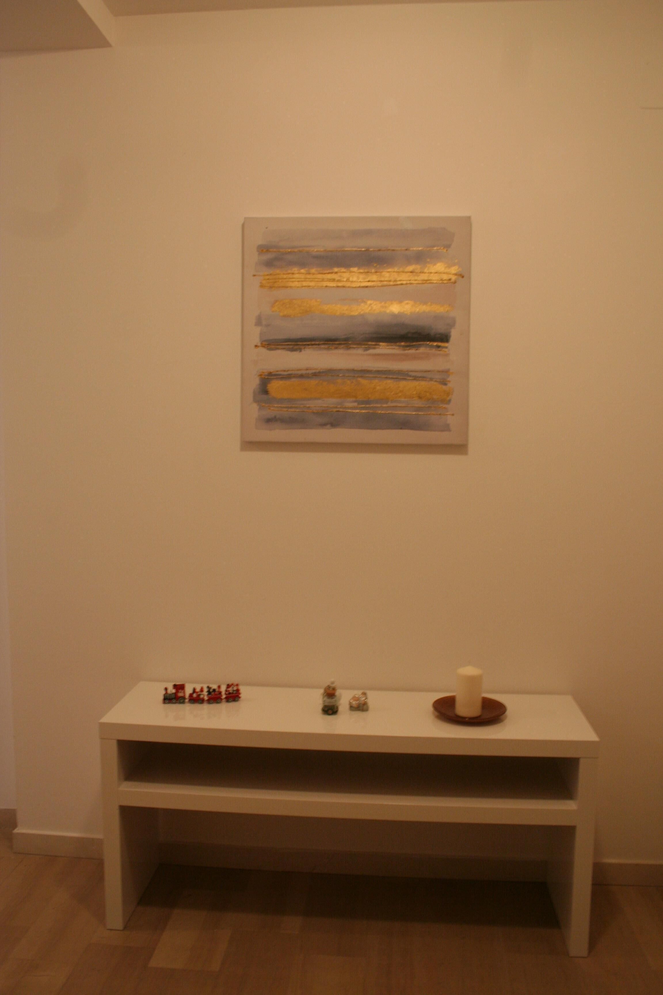A room with a white bench, a painting on the wall, and a small table with a candle.