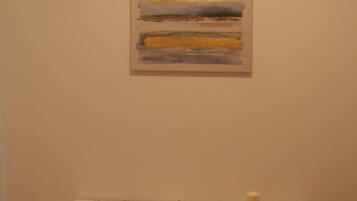 A room with a white bench, a painting on the wall, and a small table with a candle.