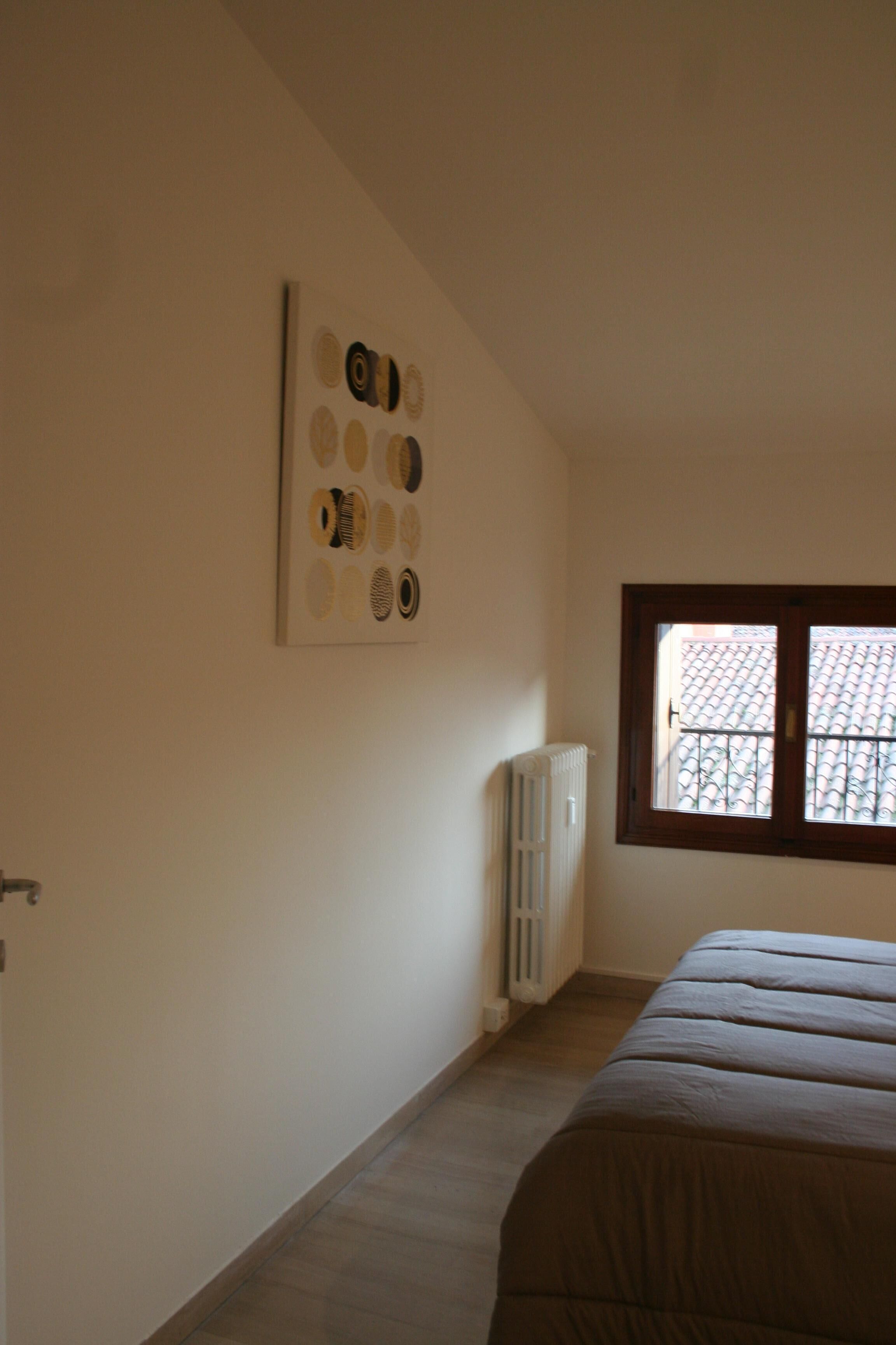 A bedroom with a bed, a radiator, a window, and a wall with circular patterns.