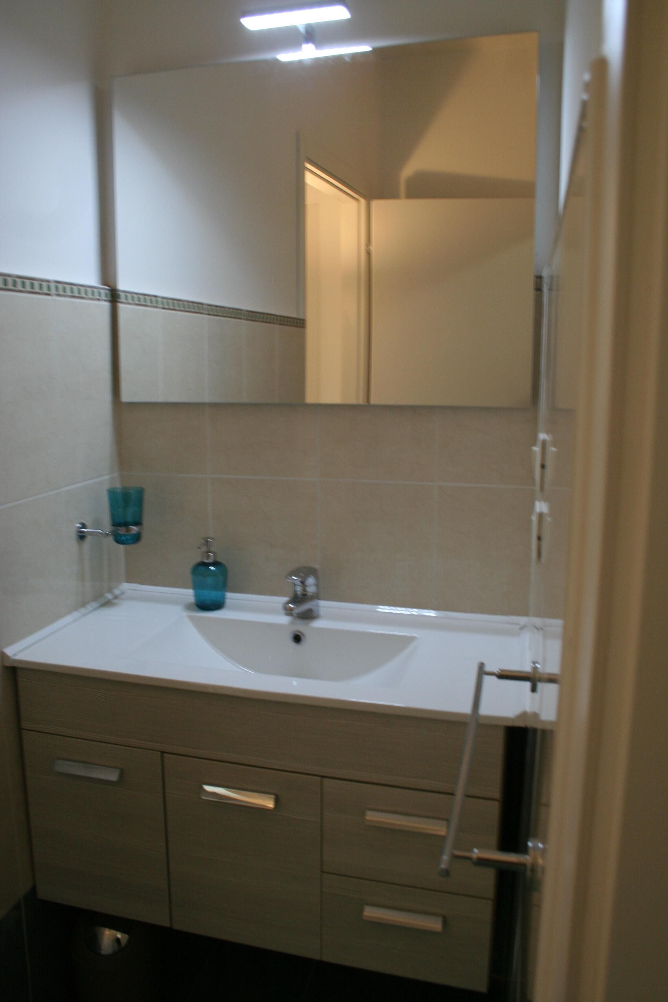 Een badkamer met een witte wastafel, een spiegel en een handdoekhouder.