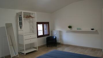 Een kamer met een bed, een kledingkast, een stoel, een radiator en een plank met spullen.
