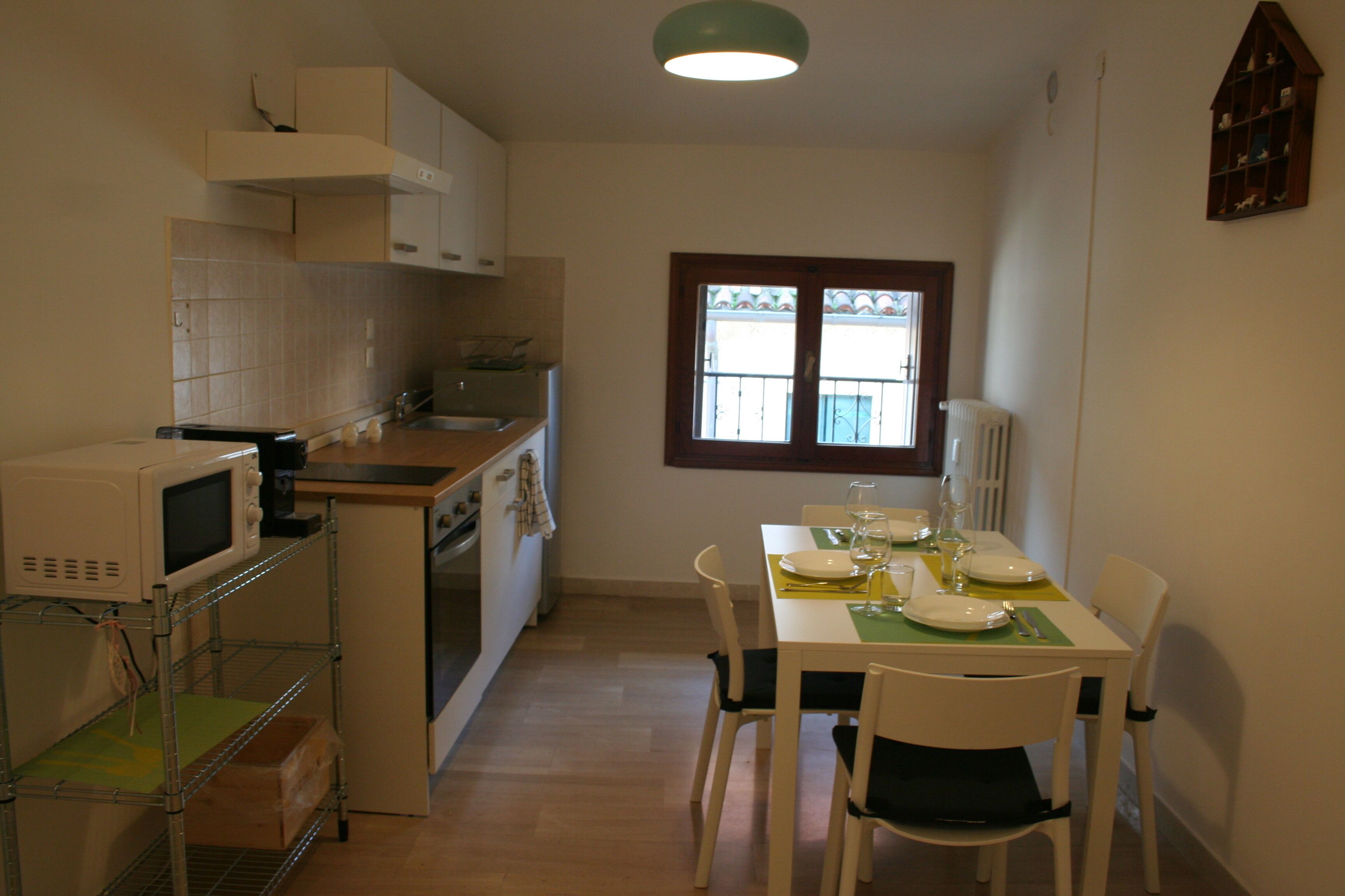 A compact kitchen with a microwave, stove, and sink. There is a dining table with chairs and a window with a view of the outside.
