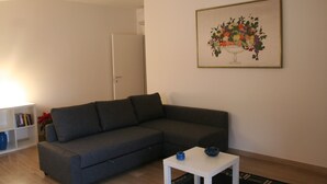 A living room with a grey sofa, a white coffee table, and a framed floral artwork on the wall. - Casa Palladio XL, in the heart of the historic city center (Vicenza)