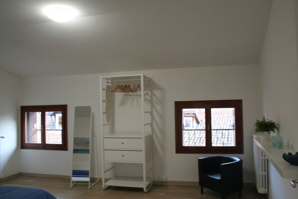 Ein Zimmer mit einem weißen Kleiderschrank, einem schwarzen Sessel und einem Fenster mit Blick auf Gebäude.