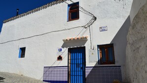 A white building with a blue door and windows, a tiled entrance, and a sign indicating a location. - Casa del Arrabal de Montefrío (Montefrio)