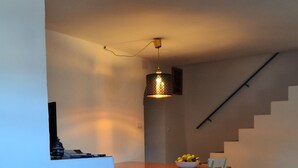 A dining area with a wooden table and chairs, a hanging light fixture, and a staircase in the background. - Casa del Arrabal de Montefrío (Montefrio)