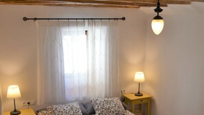 A bedroom with a bed, two bedside tables with lamps, a window with curtains, and a wooden ceiling. - Casa del Arrabal de Montefrío (Montefrio)