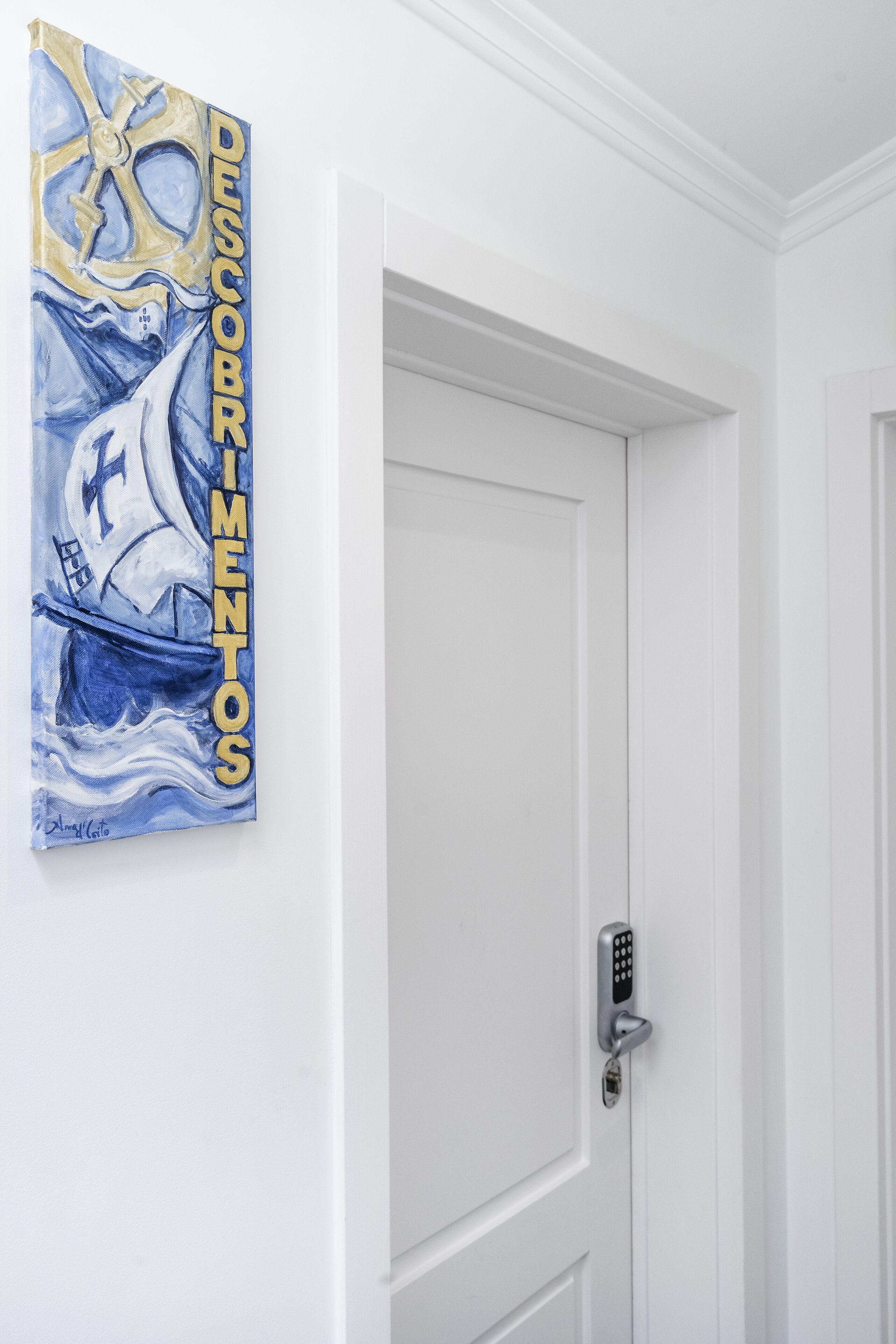 Una puerta blanca con cerradura electrónica y un cuadro de un velero en la pared.
