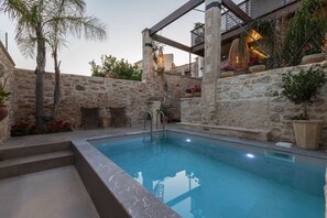 A pool area with stone walls, a pergola, and potted plants.