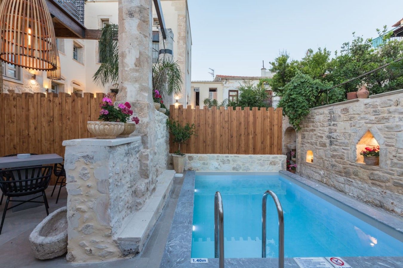A swimming pool with stone walls and wooden fences, surrounded by potted plants and outdoor furniture.