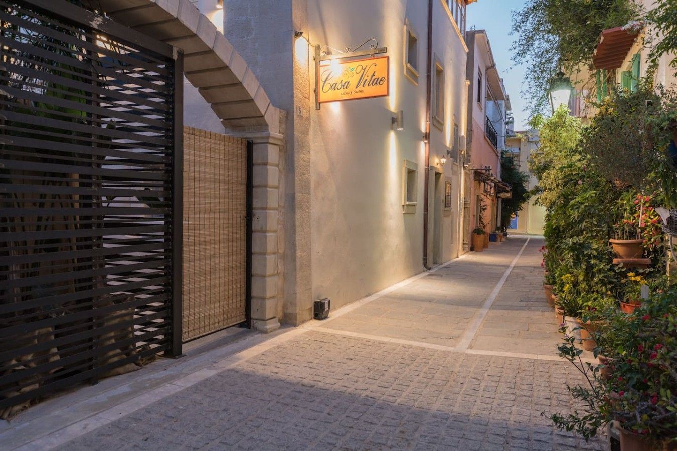 A narrow cobblestone street with a closed gate on the left and a building with a sign that reads 'Casa Vitae.'