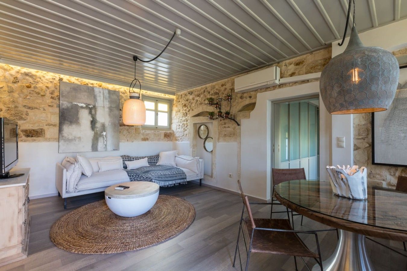 A modern living room with a stone wall, a white sofa, a round coffee table, and a dining area with a glass table and metal chairs.