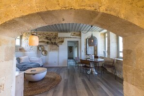 A room with a stone archway, a bed, a dining table with chairs, and a hanging light fixture.
