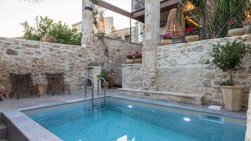 A pool area with stone walls, wicker furniture, and potted plants.