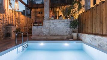 An outdoor swimming pool with a stone wall, wooden fence, and potted plants.