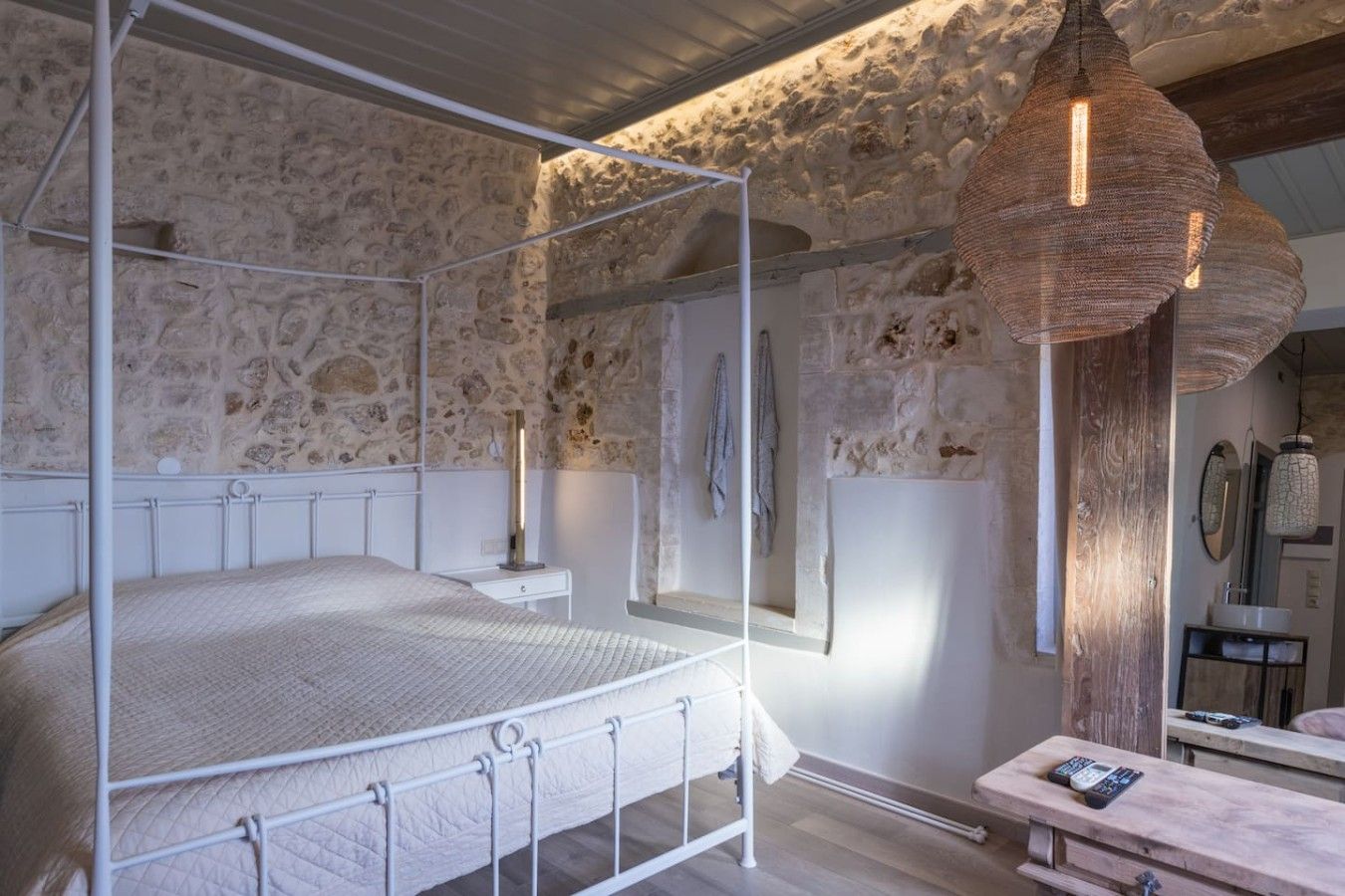 A bedroom with a four-poster bed, stone walls, a wooden bench, and a hanging light fixture.