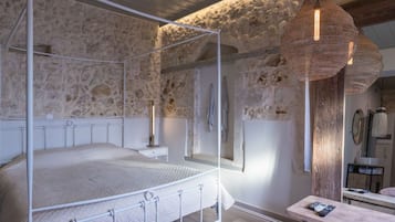 A bedroom with a four-poster bed, stone walls, a wooden bench, and a hanging light fixture.