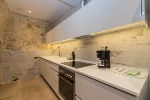 A modern kitchen with a white countertop, stainless steel appliances, and a stone wall.