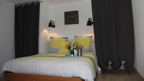 A neatly made bed with a white and gray striped bedspread, a bouquet of flowers, and a bottle of champagne. - House "Ile d'Aix" adapted PMR single center Rochefort (Rochefort)