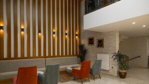 Un vestíbulo moderno con techo alto, pared de listones de madera con iluminación integrada, zona de estar con sillas coloridas, planta en maceta y radiador.