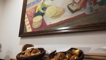 A room with a painting of women working on a textile, two bowls of bread on a wooden table.