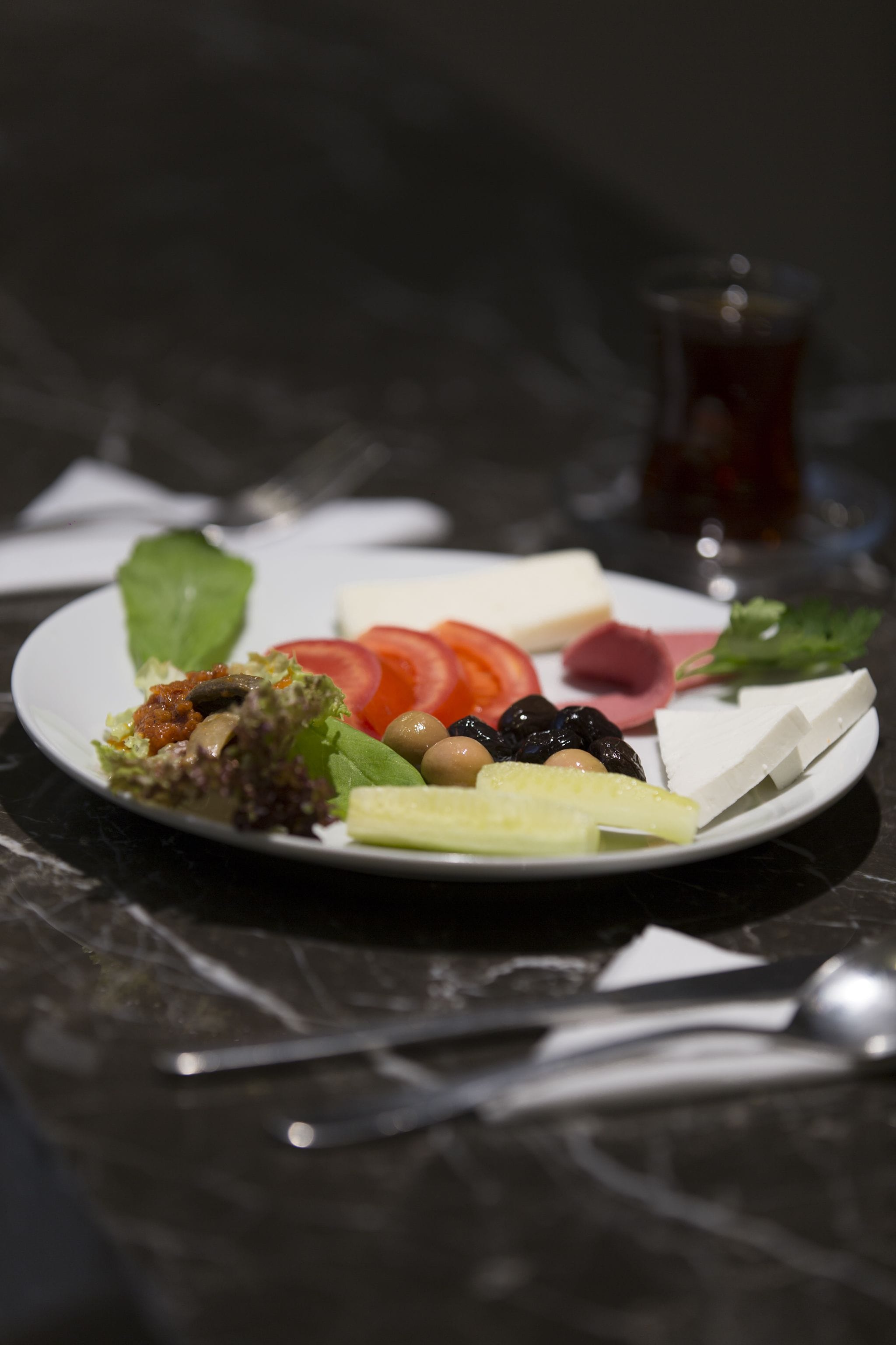 A plate of assorted cheeses, vegetables, and olives on a dark surface.