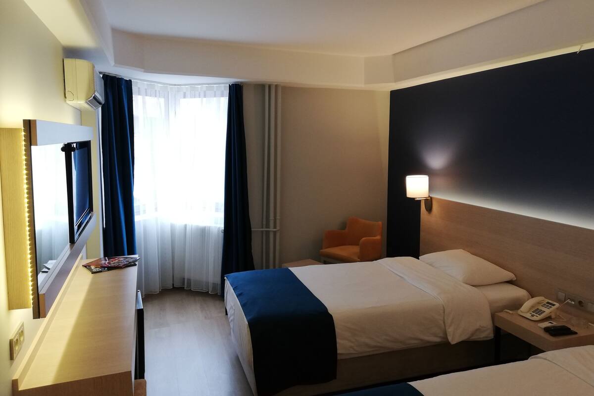 A hotel room with two beds, a desk with a telephone, a chair, a lamp, and a window with curtains.