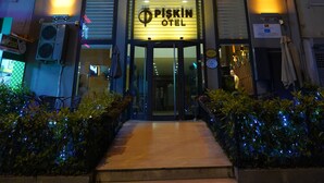 Una entrada de hotel con diseño moderno, destacando un letrero grande que dice "Piskin Hotel" y un frente bien iluminado.