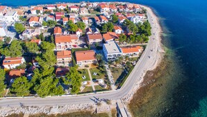 An aerial view of a coastal residential area with houses, a beach, and a clear road.
