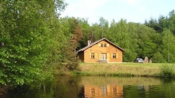 A wooden cabin by a calm lake surrounded by dense greenery. - Comfortable waterside chalet with private pond fishing in the Morvan. (Moux-En-Morvan)