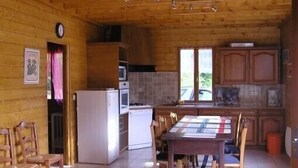 A wooden cabin interior with a kitchen, dining area, and a clock on the wall. - Comfortable waterside chalet with private pond fishing in the Morvan. (Moux-En-Morvan)