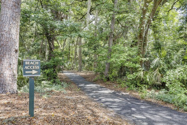 A forested path with a sign indicating beach access to the right.