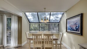 A dining area with a large window, a chandelier, and a framed painting on the wall. - Sunset Rentals | Beachwalk 110 (Hilton Head)